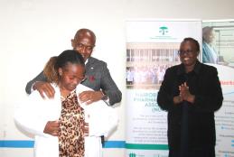 Pioneer International University VC Dr. Gideon Maina, with Prof. Faith Okalebo help a First-Year student put on her white lab coat during the White Coat Ceremony.